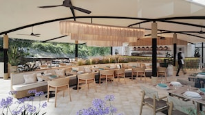 A spacious outdoor dining area with multiple seating arrangements, including sofas and tables, surrounded by natural greenery and a view of a rocky landscape.