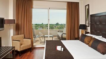A hotel room with a bed, a chair, a desk, a TV, and a balcony with a view.