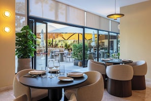 A modern dining area with round tables, cushioned chairs, and potted plants. - Senator Banús Adults Recomended (Estepona)