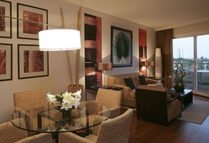 Een moderne woonkamer met een glazen eettafel, rieten meubels en een groot raam met uitzicht.