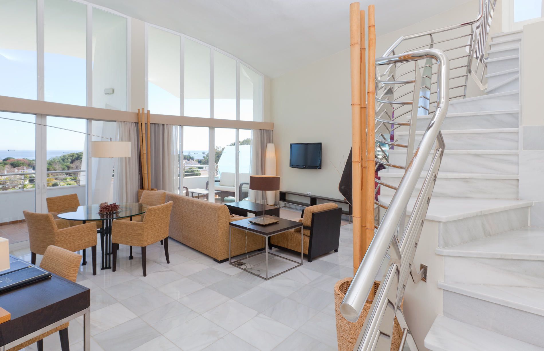 Een hotelkamer met balkon, een bank, een eettafel, een televisie en een trap.