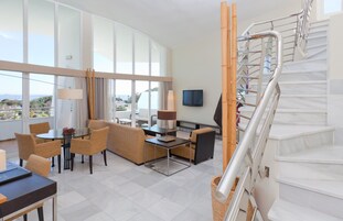 Een hotelkamer met balkon, een bank, een eettafel, een televisie en een trap.