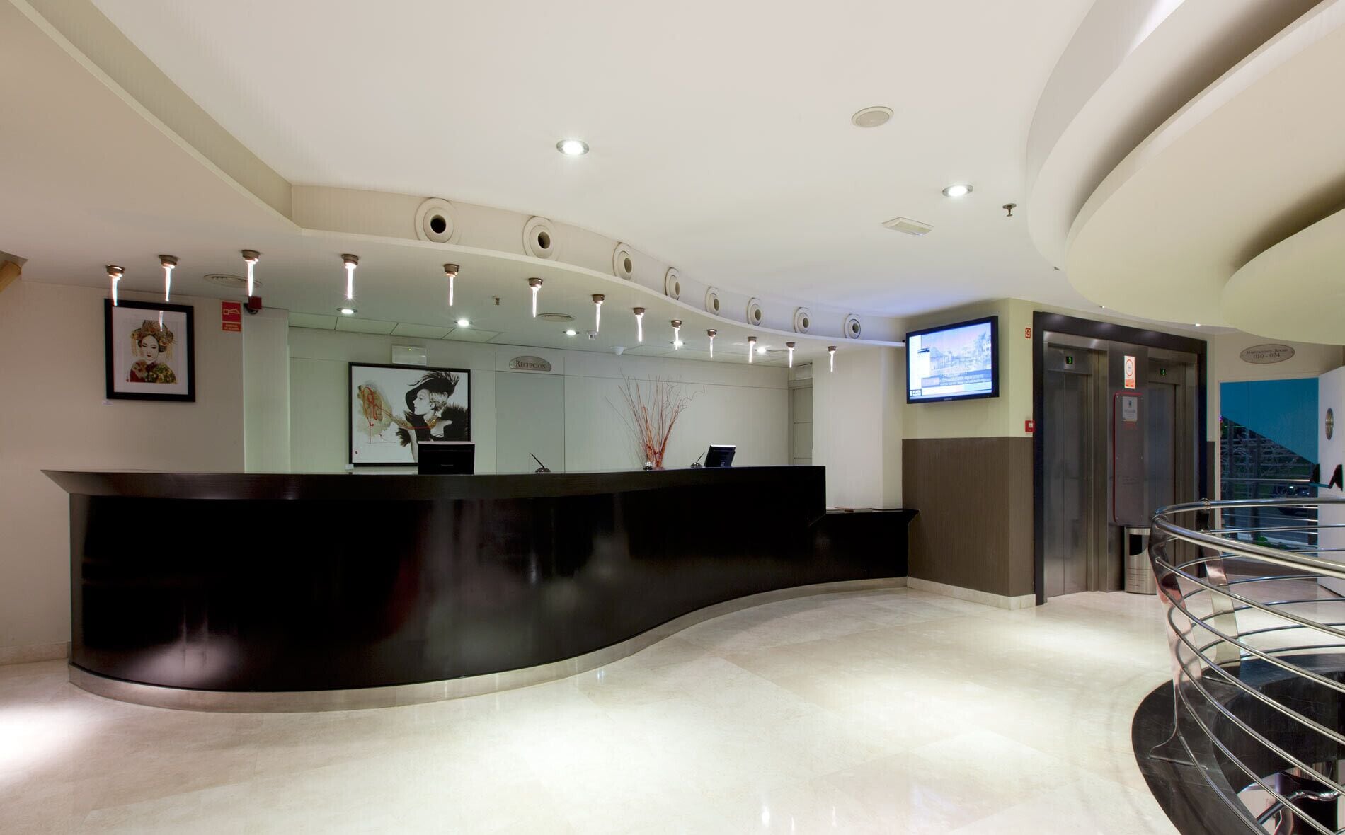 A modern reception area with a curved black counter, recessed lighting, a television mounted on the wall, and a staircase to the right.