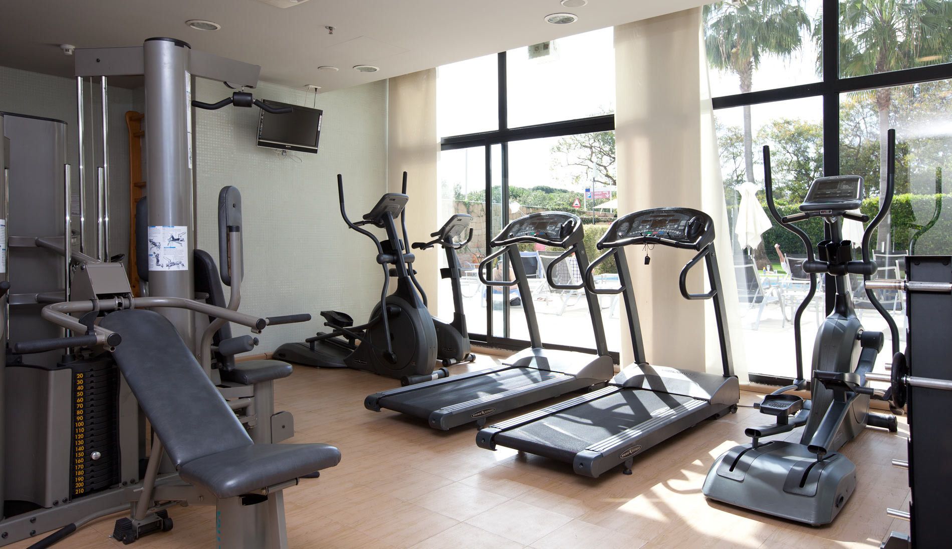 Un gimnàs amb màquines de cardio, aparells de musculació i una pantalla de televisió.