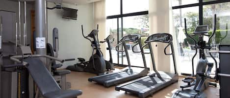 A gym with cardio machines, weight machines, and a TV screen.