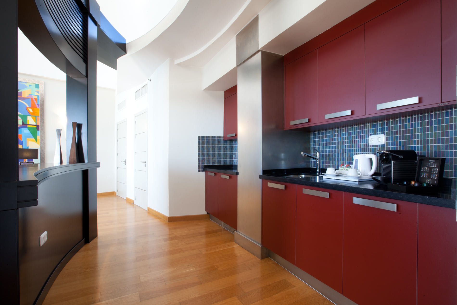 A modern kitchen with red cabinets, a black countertop, and a tiled backsplash.
