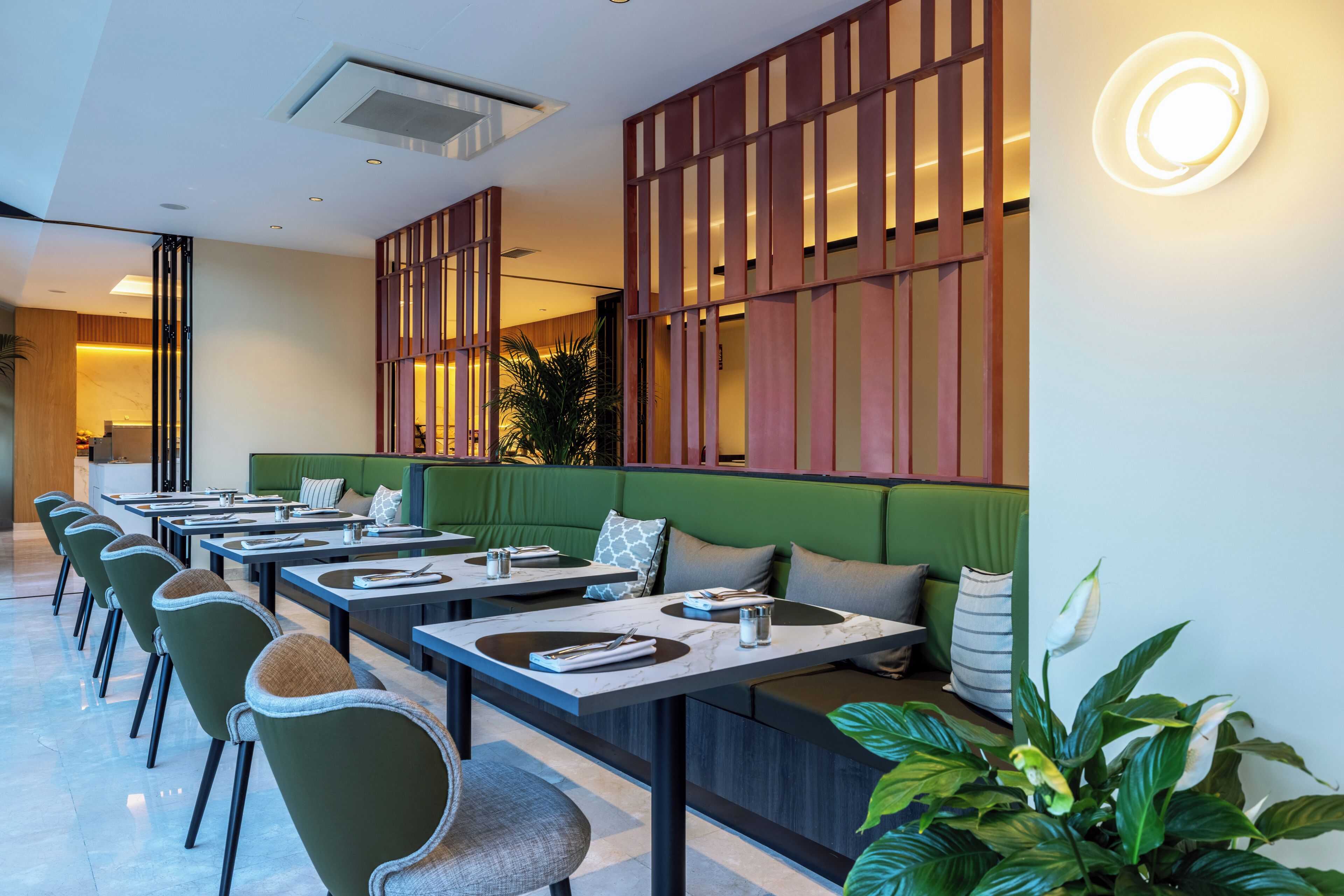 Um restaurante moderno com mesas compridas, assentos estofados verdes e uma parede decorativa com painéis verticais.
