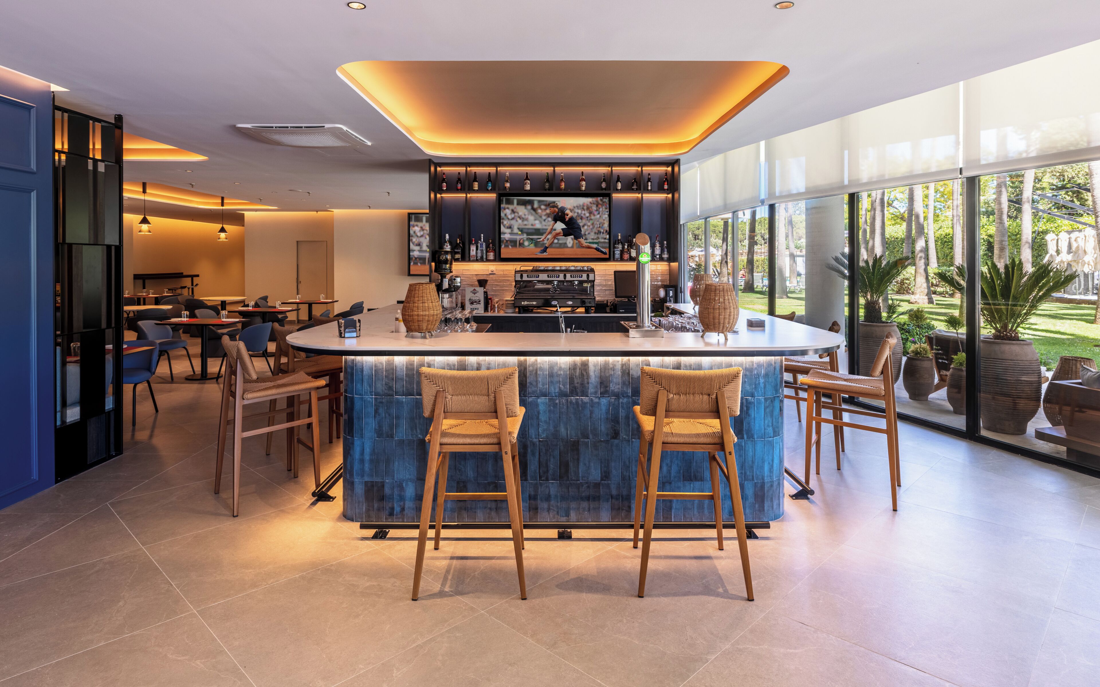 A modern bar area with a large TV screen, bar stools, and a view of the outdoors.