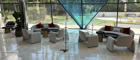 A modern lounge with a glass wall, contemporary furniture, and a view of a landscaped garden.