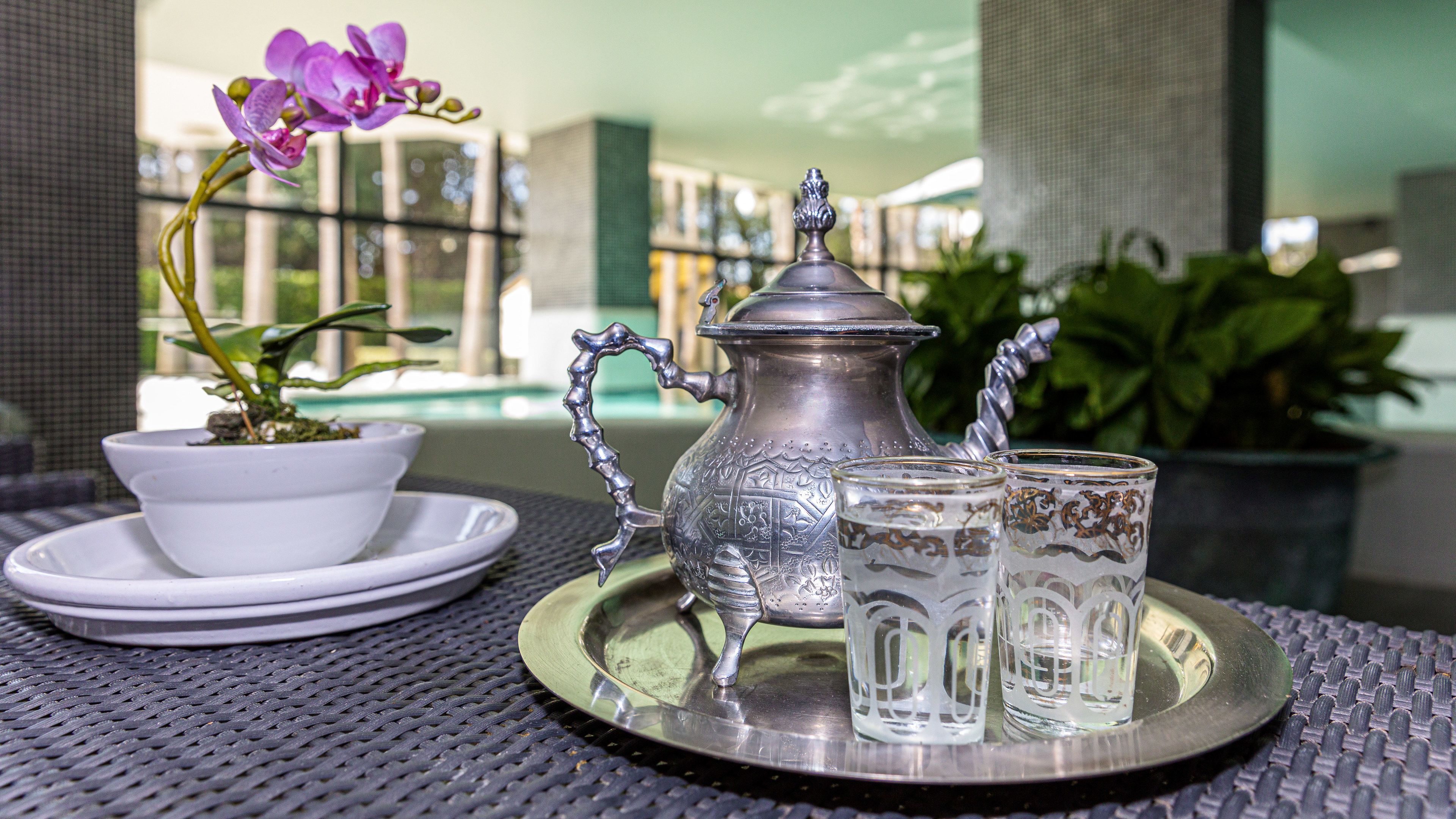 A tray with a silver pitcher, two glasses, and a potted orchid on a table.