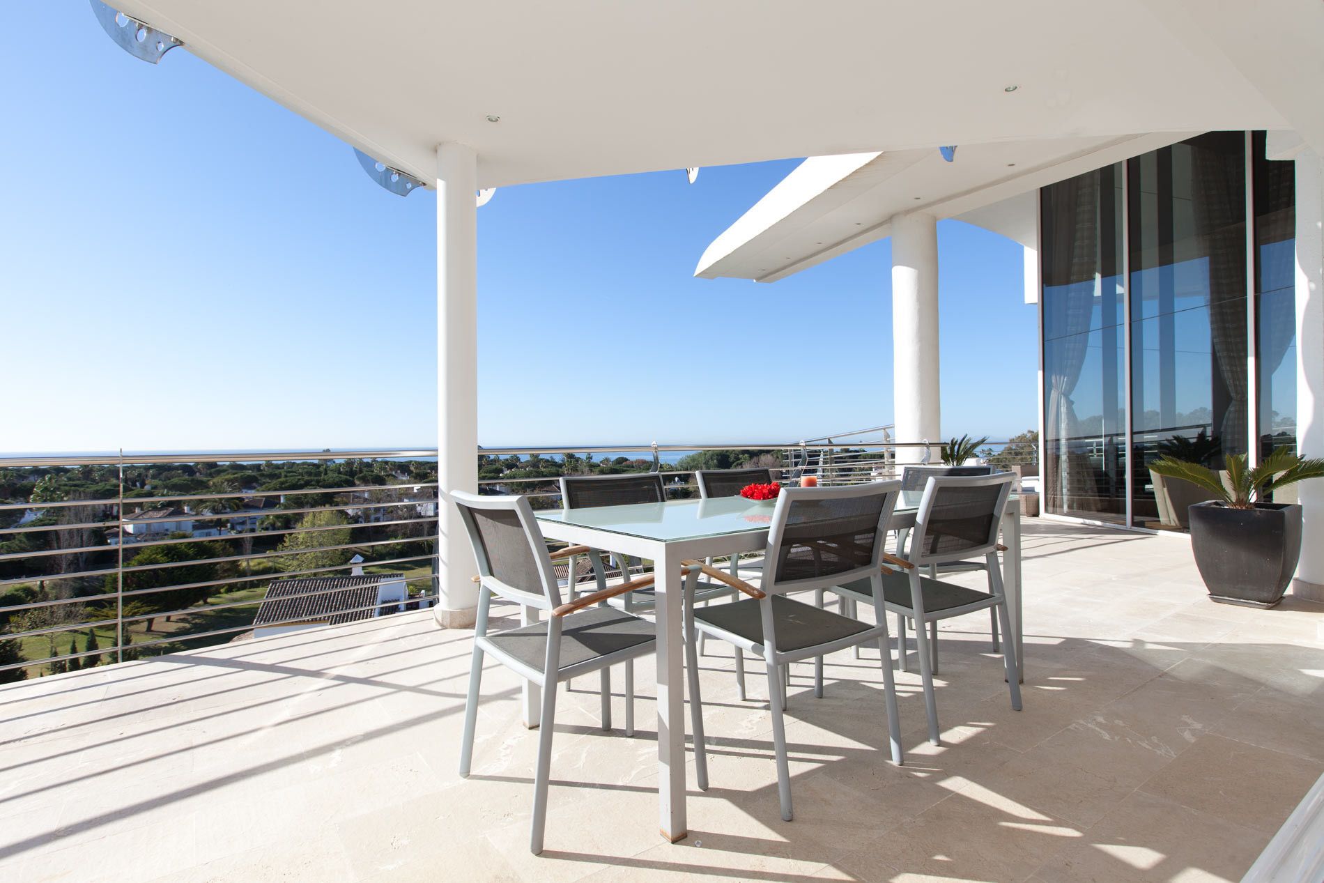 A balcony with a glass table and chairs, overlooking a residential area.