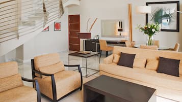 Una sala moderna con una escalera, un conjunto de sofá, una mesa de centro, un escritorio y un televisor.