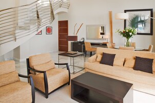 A modern living room with a staircase, a sofa set, a coffee table, a desk, and a television.
