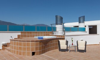 Een dakterras met een bubbelbad, twee stoelen, een tafel en uitzicht op zee en bergen.