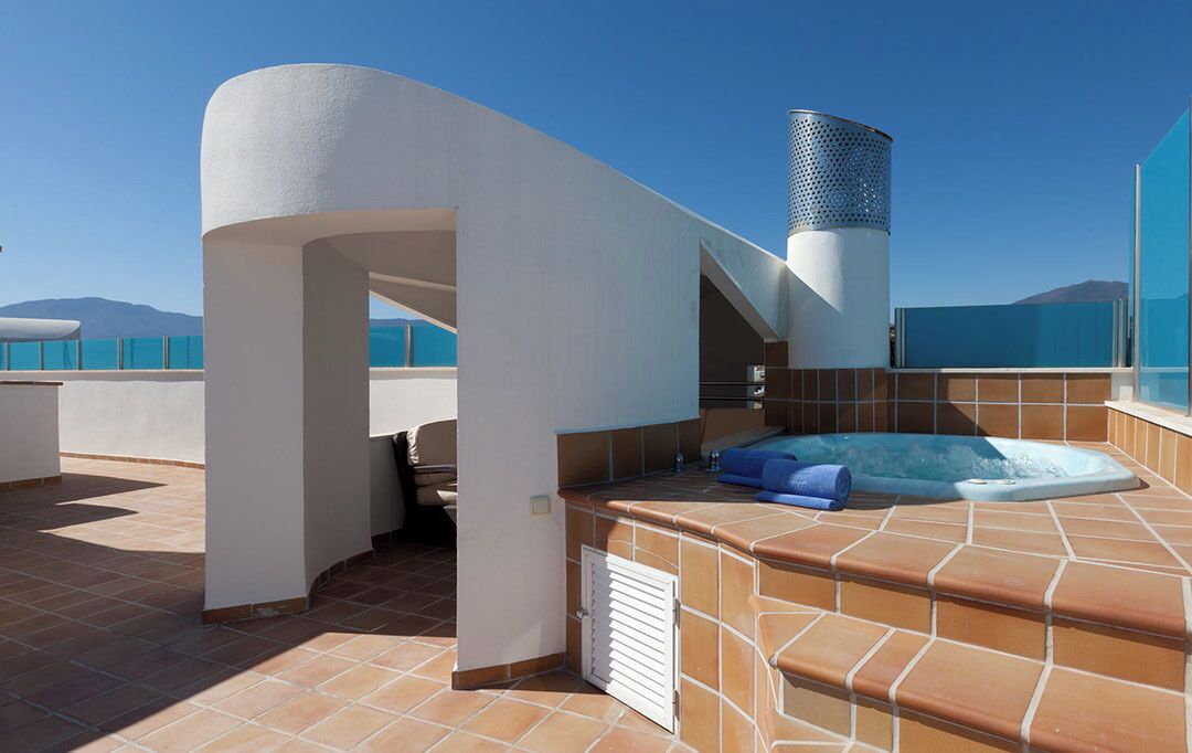 A rooftop terrace with a hot tub, a covered seating area, and a view of the sea.