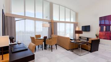 Habitación de hotel con un amplio ventanal, sofá, mesa de comedor y televisión.
