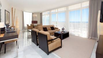 Una habitación de hotel moderna con sofá, sillones, una mesa de comedor y una televisión.