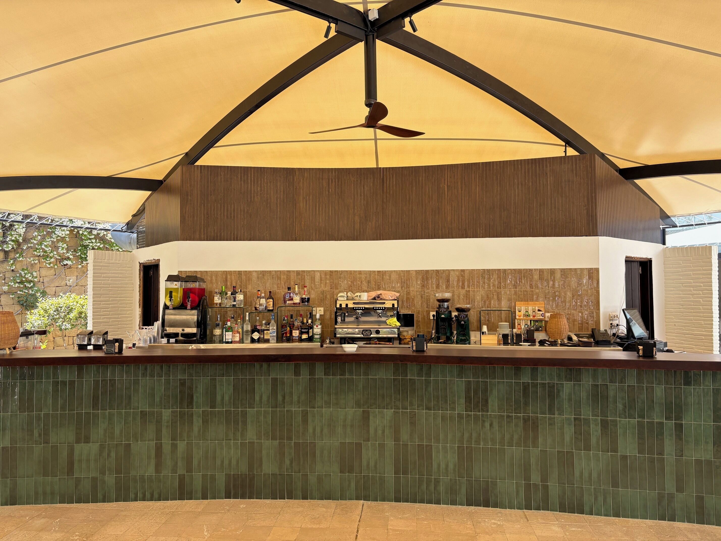 Un'area bar con una ventola a soffitto, un bancone con diversi tipi di bottiglie e una parete rivestita di piastrelle.