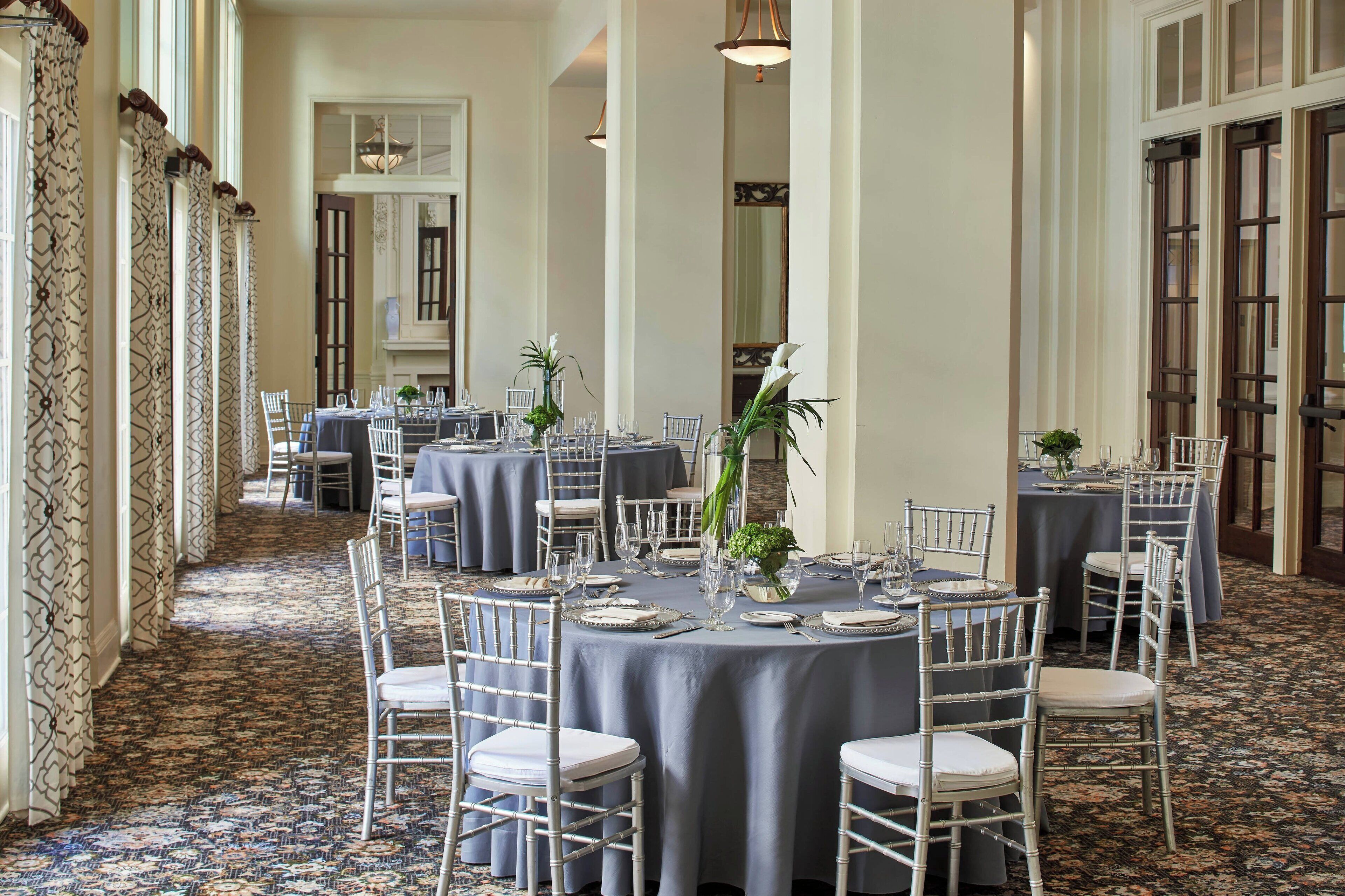 A formal dining area with round tables, white chairs, and blue tablecloths.
