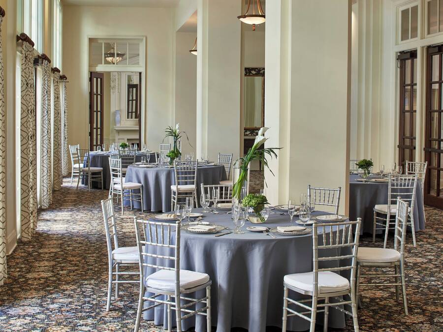 A formal dining area with round tables, white chairs, and blue tablecloths.