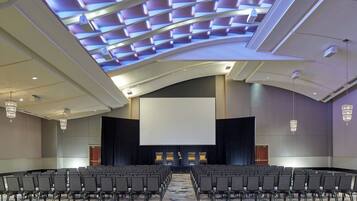 A large conference room with rows of chairs, a large screen, and a modern ceiling design.