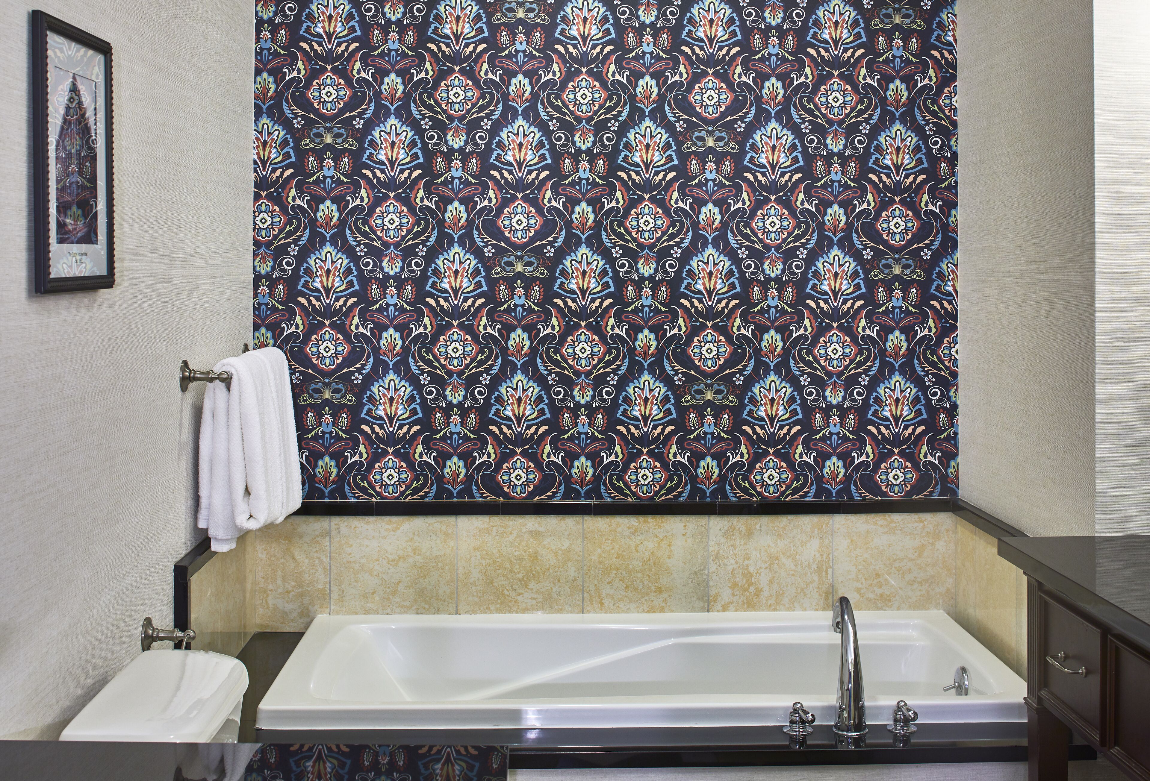 A bathroom with a large bathtub, a towel rack with a white towel, and a patterned tile backsplash.