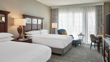 A hotel room with two beds, a desk, a chair, a TV, and a window with curtains.