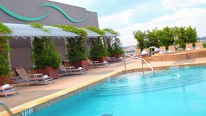 A swimming pool with lounge chairs and umbrellas, surrounded by greenery and a building with a wave-like design. - The Battle House Renaissance Mobile Hotel & Spa (Mobile)