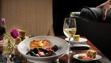 A dining table with a bowl of mussels, a glass of white wine, and bread.