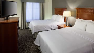 A hotel room with two beds, a TV, a lamp, and a window with curtains.