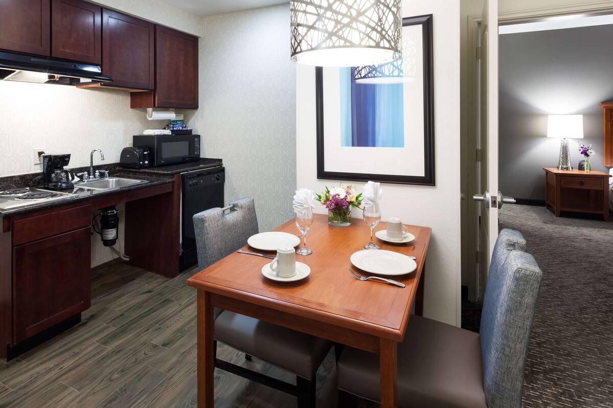Une chambre d’hôtel compacte comprenant un coin cuisine, une table à manger pour deux personnes, un lit et une salle de bain.