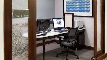 A business center with two computers, a printer, and a sign indicating 24-hour availability.