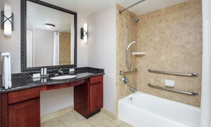 Ein modernes Badezimmer mit Marmorwaschtisch, großem Spiegel, Badewanne und Dusche inklusive Haltegriffen.