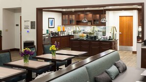 A hotel dining area with a long communal table, individual tables, and a seating area with a sofa. - Homewood Suites by Hilton Agoura Hills (Agoura Hills)