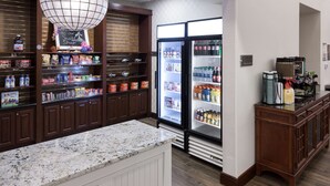 A kitchen area with a marble countertop, a refrigerator stocked with beverages, and shelves with snacks and condiments. - Homewood Suites by Hilton Agoura Hills (Agoura Hills)