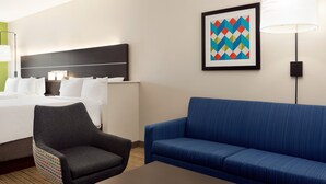 Ein Hotelzimmer mit einem Bett, einem blauen Sofa, einem Sessel, einer Lampe und einem gerahmten Bild an der Wand.