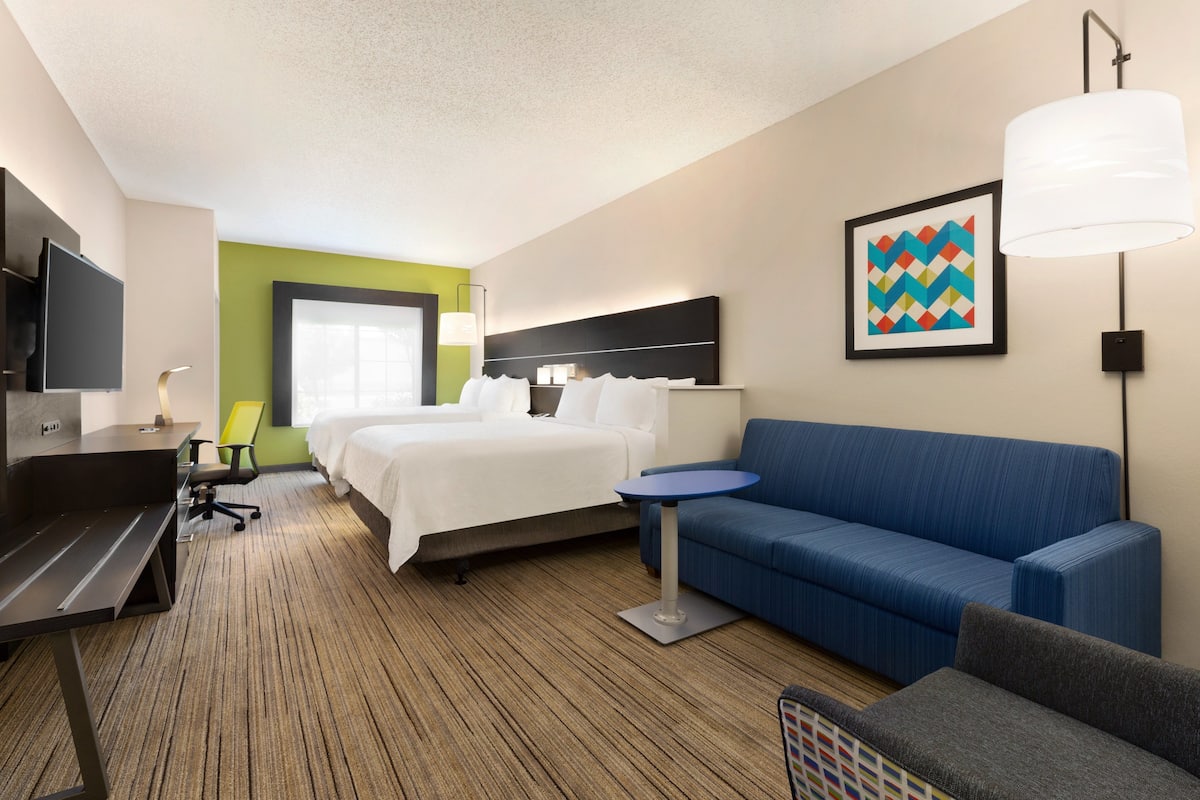 Una habitación de hotel con una cama, un sofá azul, un escritorio con una silla, un televisor y una lámpara.