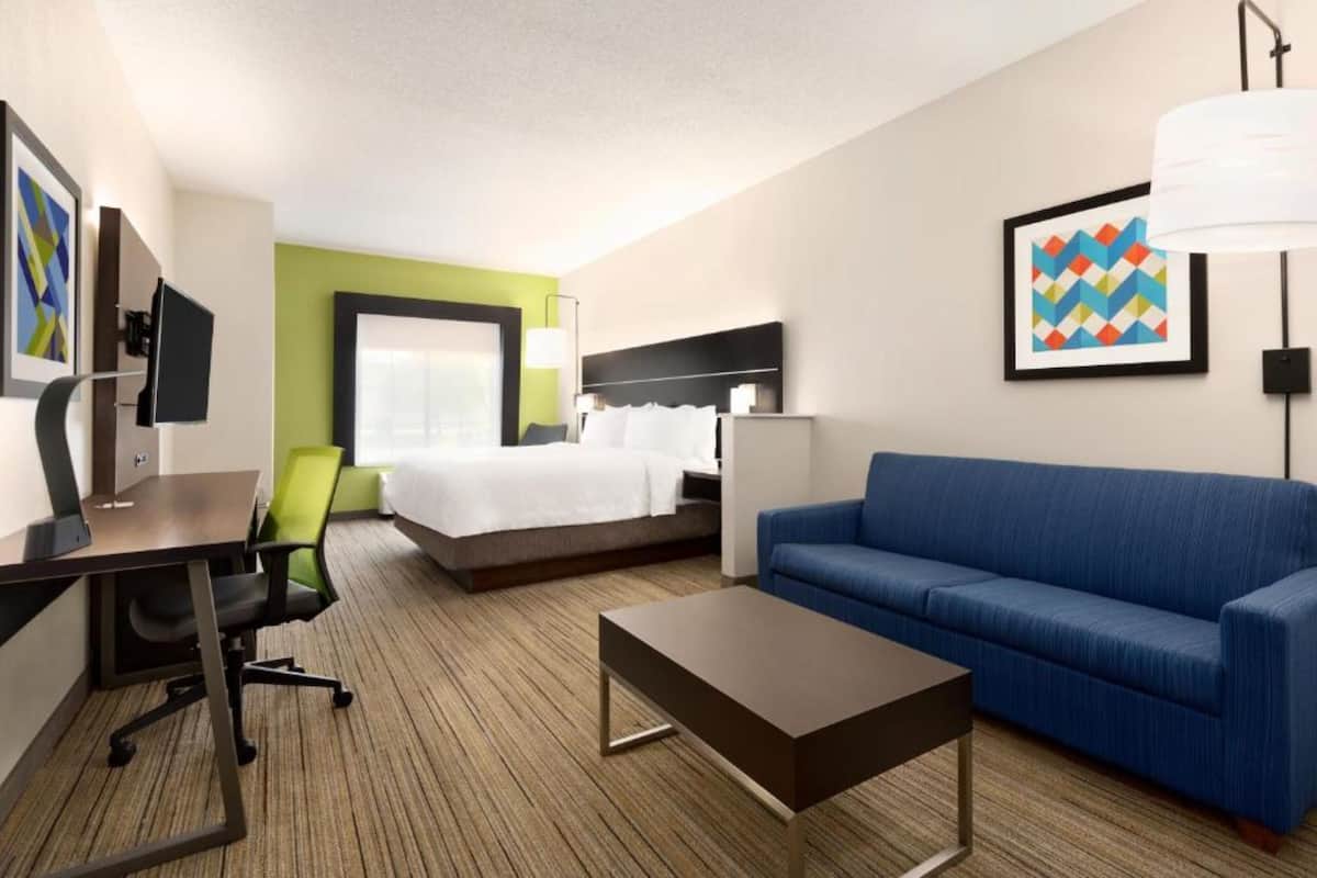 Una habitación de hotel con una cama, un sofá azul, un escritorio con una silla, una mesa de centro y un televisor.