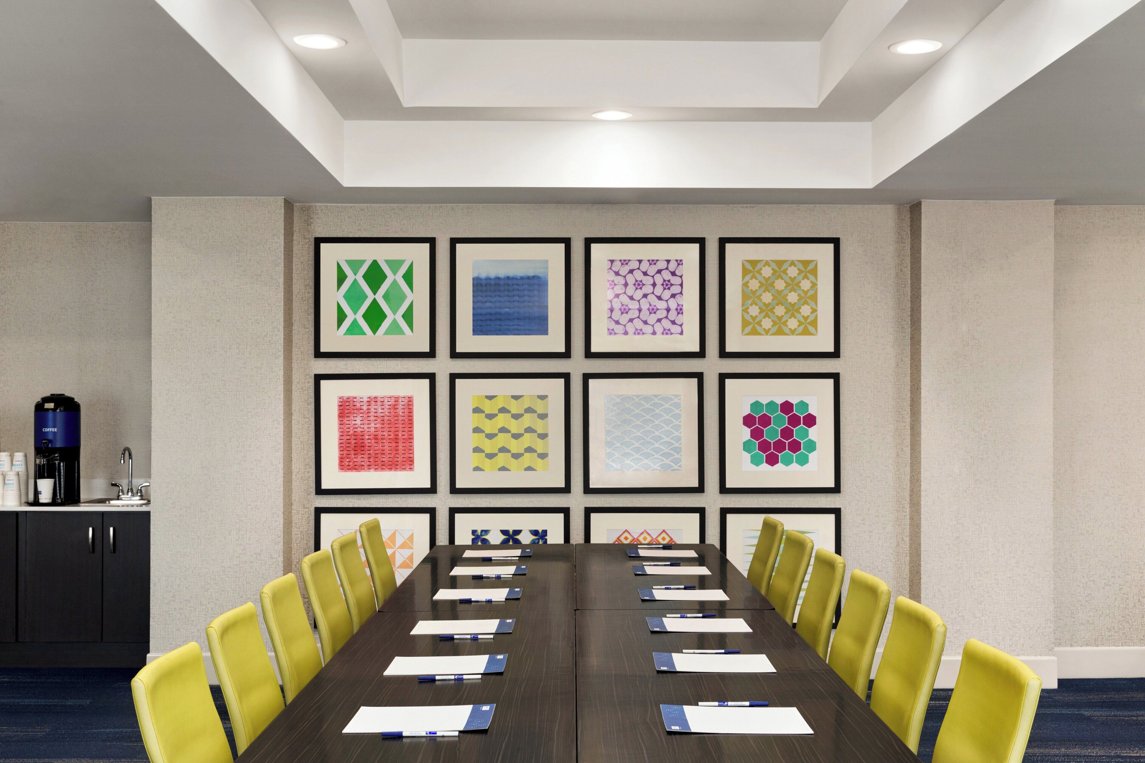 A conference room with a long table, yellow chairs, and framed artwork on the walls.