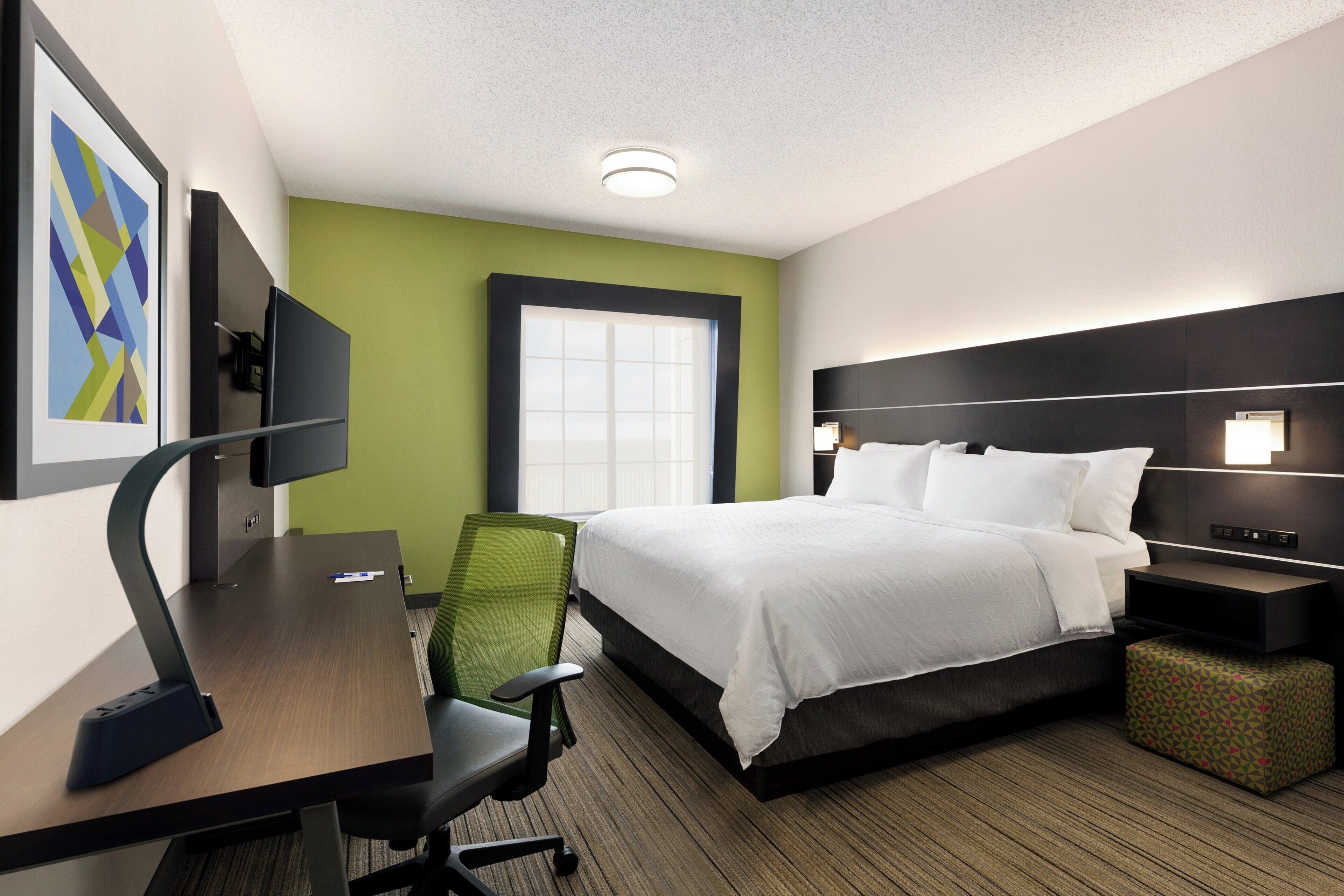 A hotel room with a bed, desk, chair, and a television on the wall.