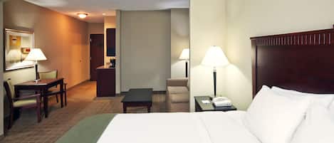 Habitación de hotel con una cama, dos mesitas de noche con lámparas, un escritorio con una silla y una pequeña mesa con otra silla.