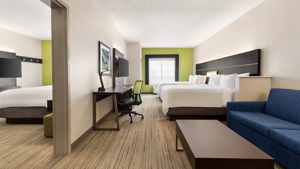 Ein Hotelzimmer mit zwei Betten, einem Schreibtisch, einem Sessel, einer Couch und einem Fernseher.