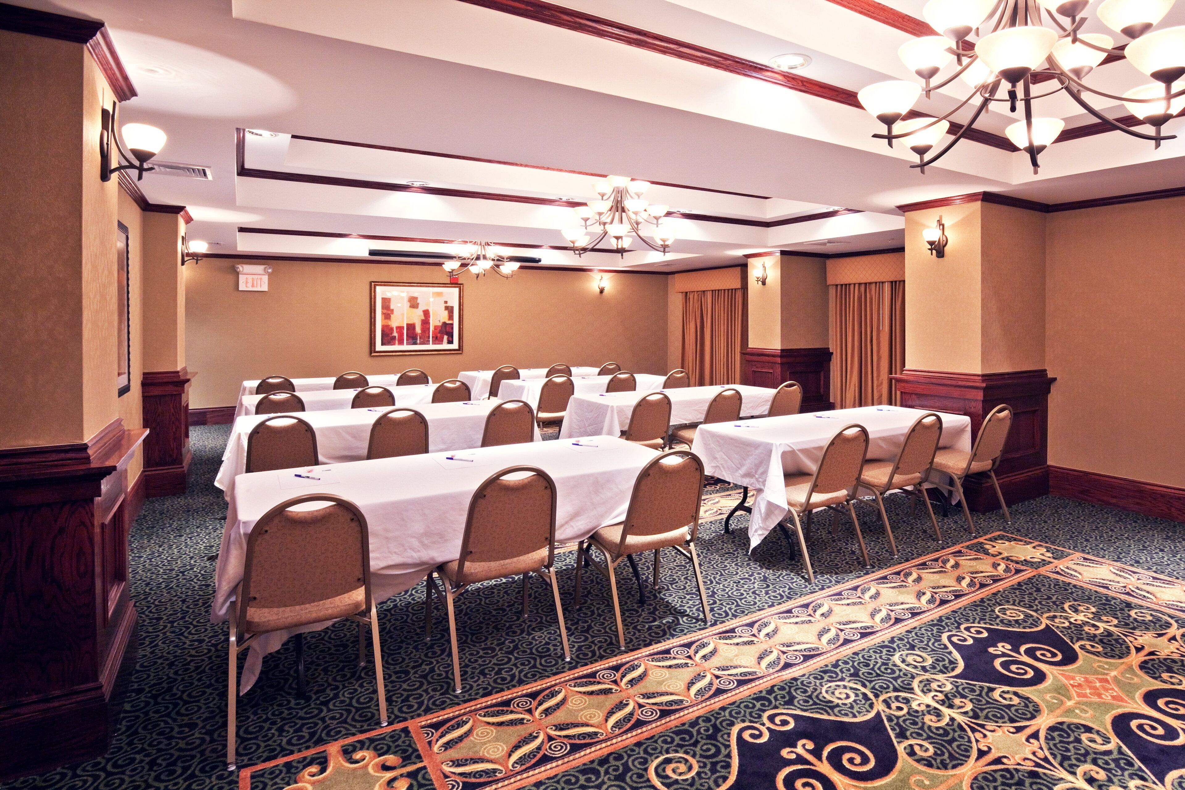 Sala de conferências com várias mesas e cadeiras, piso coberto por carpete e um candelabro.