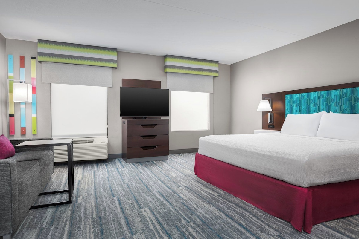 A hotel room with a bed, a desk, a television, and a window.