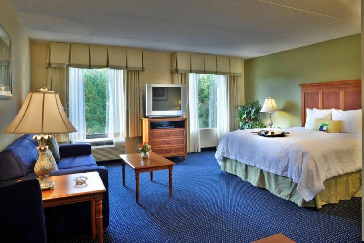 A hotel room with a bed, a TV, a desk, a chair, and a sofa.