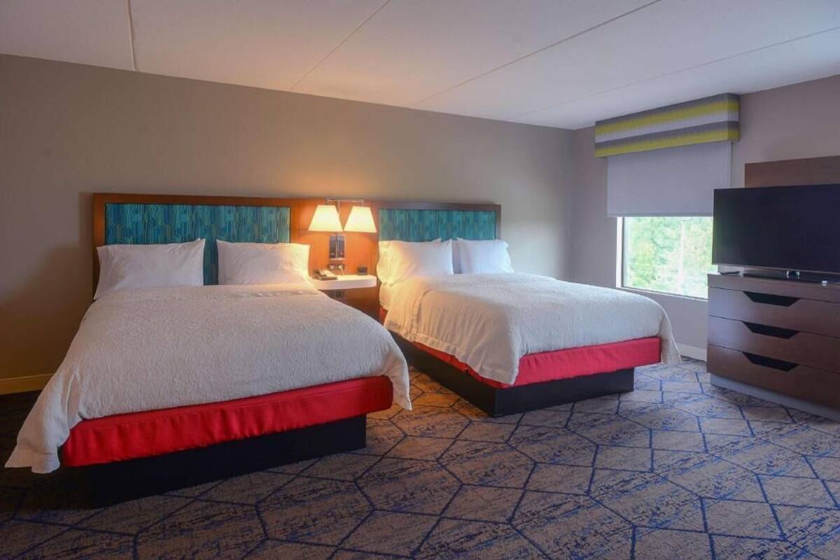 A hotel room with two beds, a TV, a dresser, and a window.
