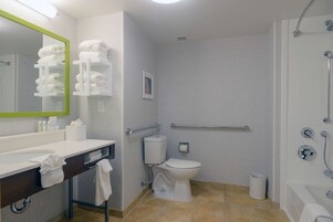 Un baño moderno con lavamanos, inodoro y ducha blancos. Hay toallas en el mostrador y un espejo con marco verde.