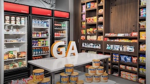 Ein Supermarkt mit Kühlregalen, Regalen voller Snacks und Getränke sowie einem gut sichtbaren 'GA'-Schild.