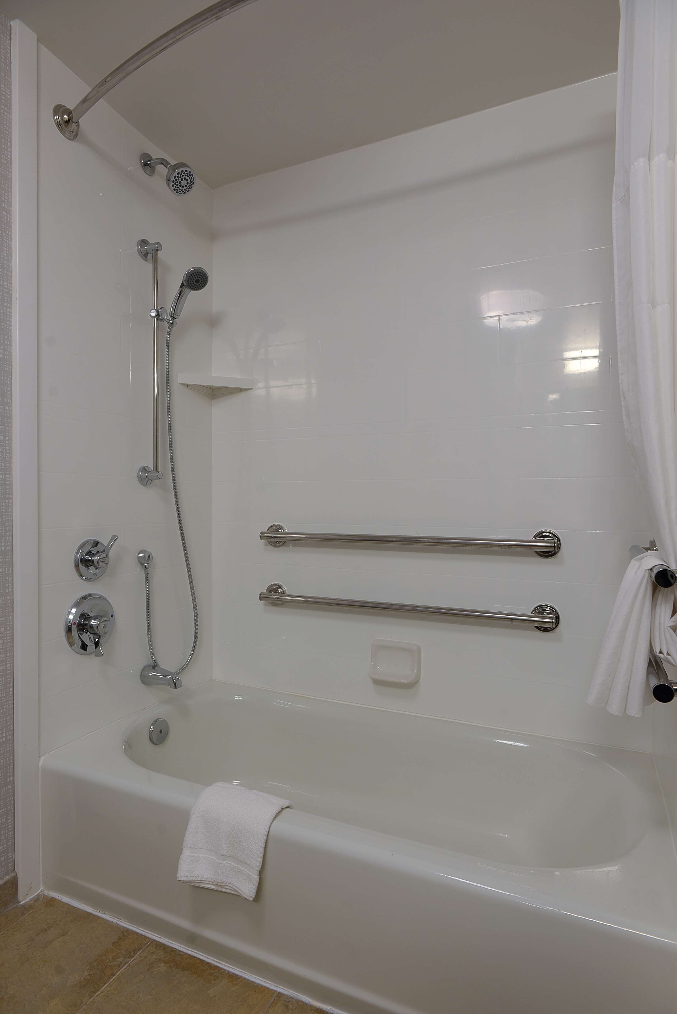 A modern bathroom with a bathtub, a shower area, and grab bars for safety.