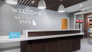 Ein Empfangsschalter mit einem Schild, auf dem "Welcome to the Peach State" steht, einem Hilton Honors-Schild und einem Snackautomaten.